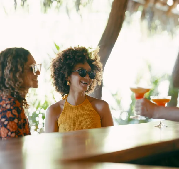 Two women enjoying cocktails at an outdoor resort bar on a sunny day.