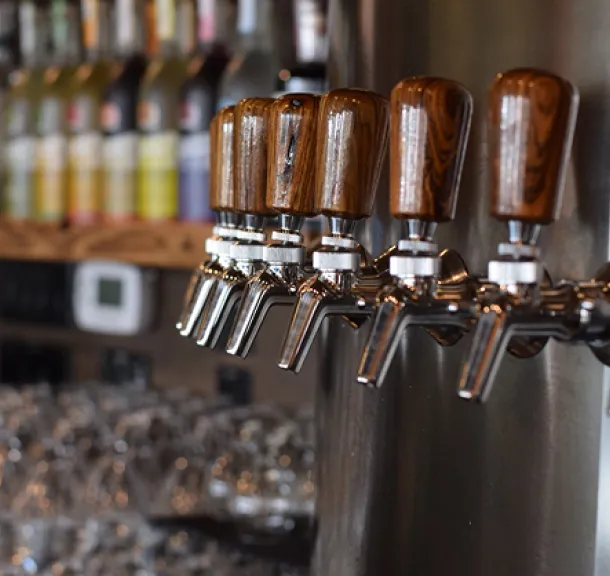 Row of wood-handled draft beer taps at a resort bar with liquor bottles in background.