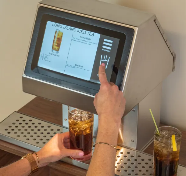 Touchscreen cocktail dispenser machine pouring a Long Island Iced Tea with recipe instructions on screen.